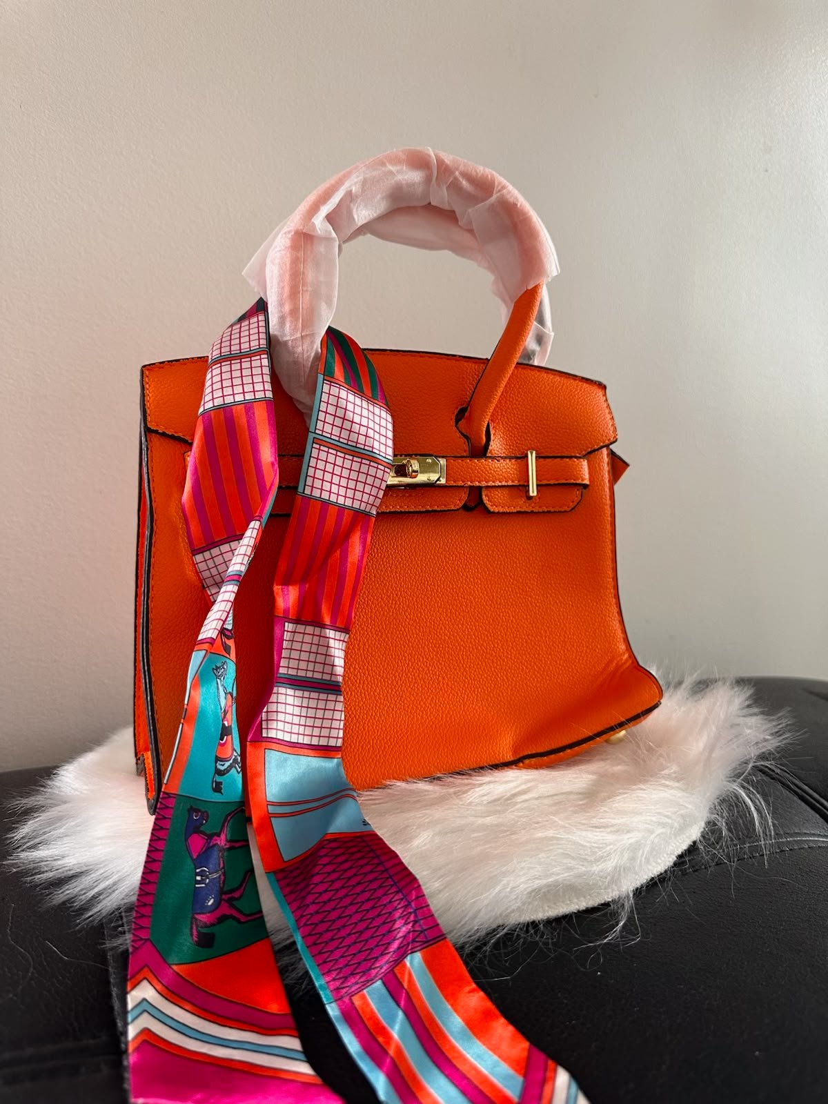Sac à main structuré Élégant sac à main structuré orange avec doubles poignées, détails métalliques dorés et foulard imprimé coloré. Un modèle audacieux et raffinéorange avec foulard imprimé